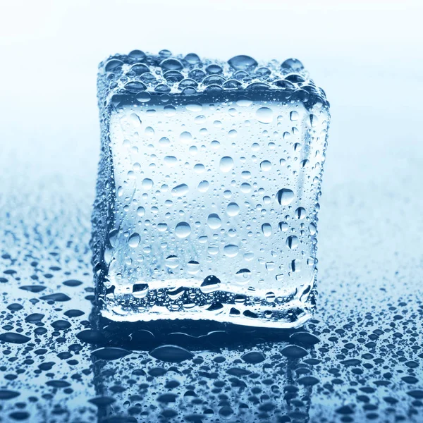 Cubo de gelo transparente com reflexão em vidro azul com gotas de água — Fotografia de Stock