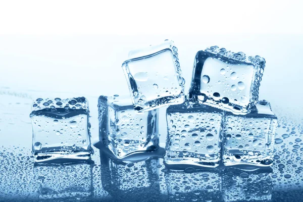 Grupo de cubos de gelo transparente com reflexão em vidro azul com gotas de água — Fotografia de Stock
