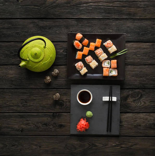 Set di sushi e rotoli con teiera su legno nero rustico, vista dall'alto — Foto Stock