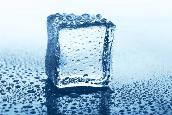 Transparante ijsblokje met reflectie over blauw glas met water druppels — Stockfoto