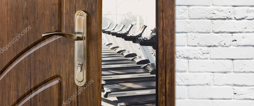 Entrance to gym in fitness club, opened door with treadmills