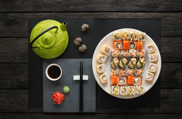 Sada sushi a rohlíky s konvicí na černé rustikální dřevo, horní pohled — Stock fotografie