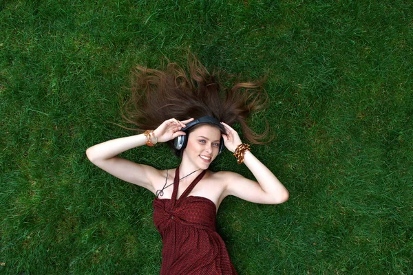Pretty young girl listen music in headphones lying on grass — Stock Photo, Image