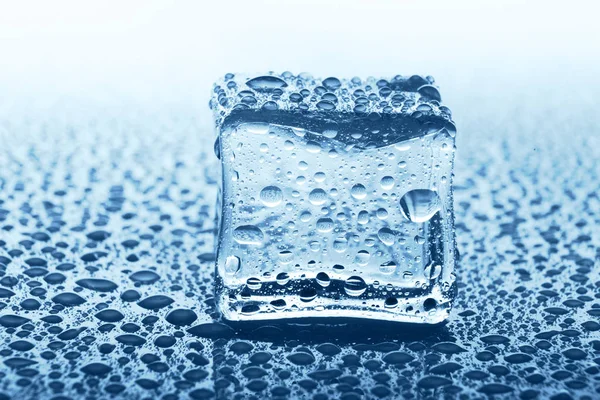 Cubo de gelo transparente com reflexão em vidro azul com gotas de água — Fotografia de Stock