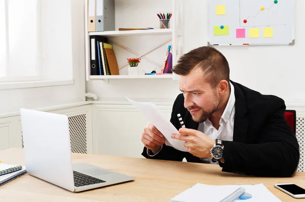 Junger konzentrierter Geschäftsmann liest Dokumente in modernem weißen Büro — Stockfoto