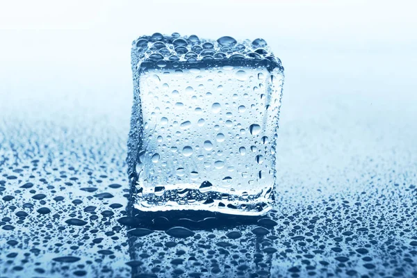 Transparentní ice cube s odrazem na modré sklo s vodou kapky — Stock fotografie
