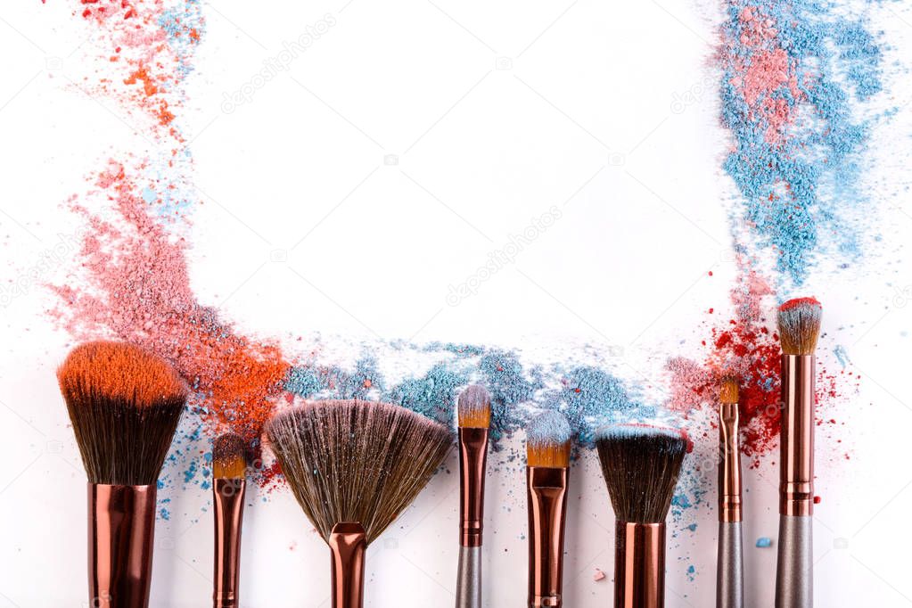 Makeup brushes with blush or eyeshadow of pink, blue and coral tones sprinkled on white background