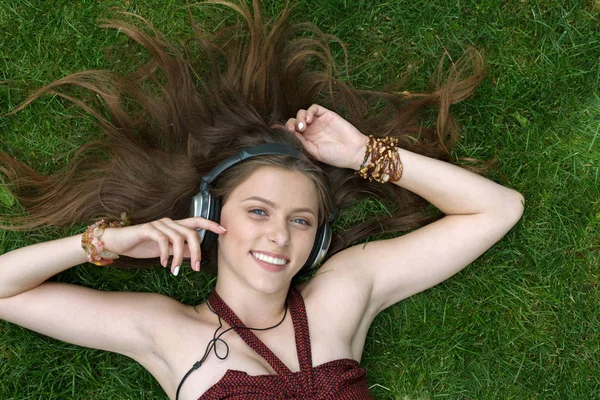 Menina bonita ouvir música em fones de ouvido deitado na grama — Fotografia de Stock