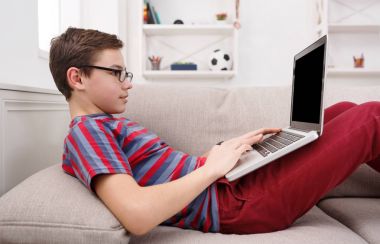 Genç çocuk evde kanepede dizüstü bilgisayar kullanarak