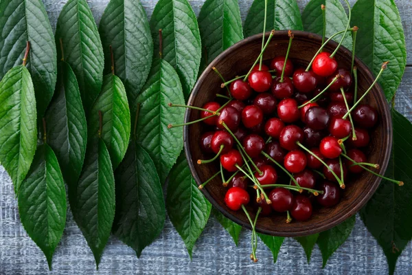 Süße frische Kirschen mit grünen Blättern auf blauem, rustikalem Holz — Stockfoto