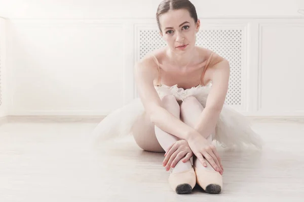 Крупный план молодой балерины сидеть в пуантах обувь на белом фоне пола — стоковое фото