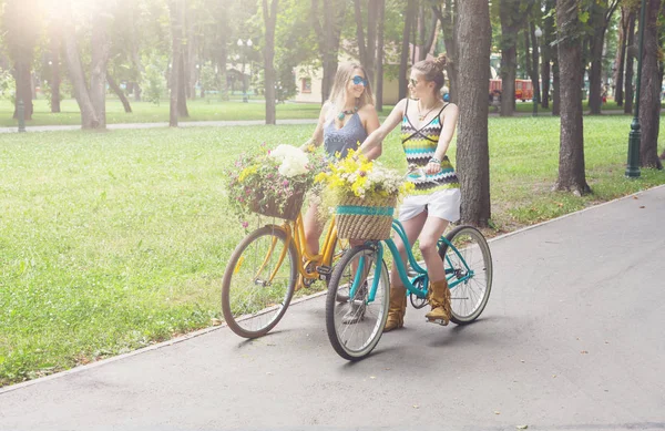 Feliz boho chic niñas paseo juntos en bicicletas en el parque —  Fotos de Stock