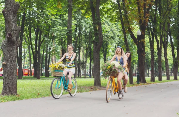 Happy boho chic girls ride together on bicycles in park — Stock Photo, Image