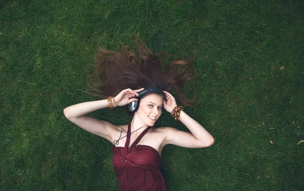 Pretty young girl listening music in headphones lying on grass — Stock Photo, Image