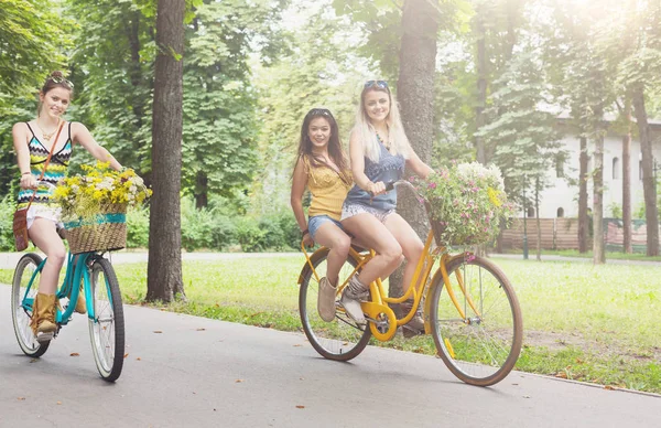 Felice boho chic ragazze cavalcare insieme su biciclette nel parco — Foto Stock