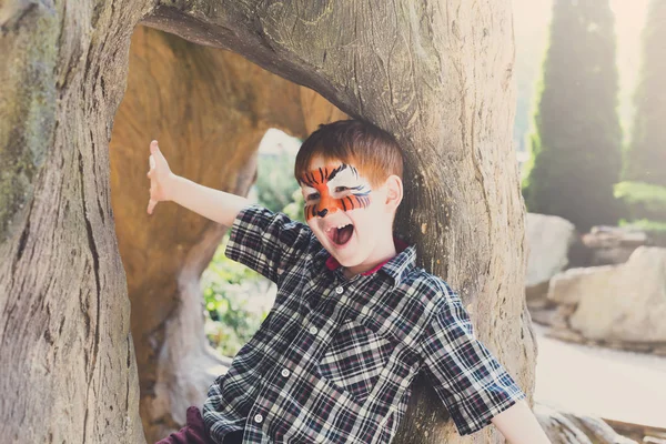 Chłopiec dziecko na zewnątrz siedzieć w drzewo z malowanie twarzy — Zdjęcie stockowe