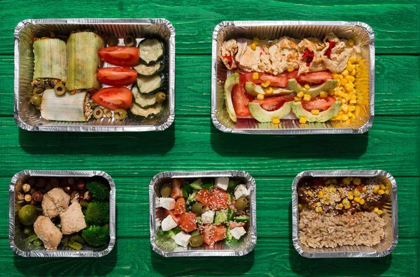 Healthy food take away in boxes, top view at green wood