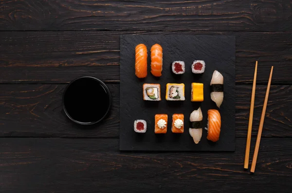 Set zalmsushi en broodjes op zwarte houten achtergrond, bovenaanzicht — Stockfoto
