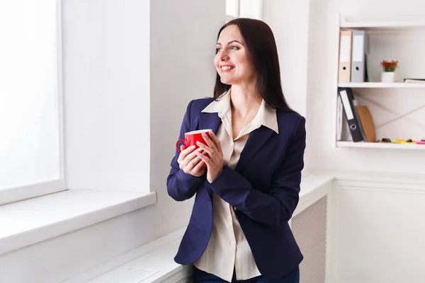 Mujer beber café cerca de la ventana en el lugar de trabajo — Foto de Stock