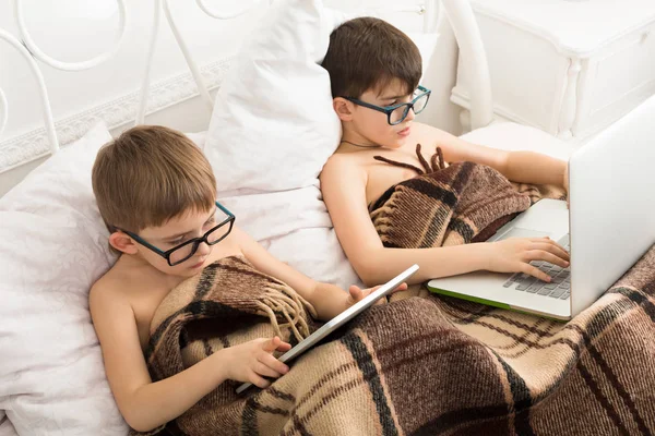 Два мальчика играют в ноутбук и планшет с собакой в постели — стоковое фото