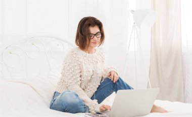 Genç kadın serbest meslek ile yatakta, yüksek anahtar laptop