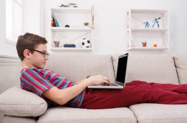 Genç çocuk evde kanepede dizüstü bilgisayar kullanarak