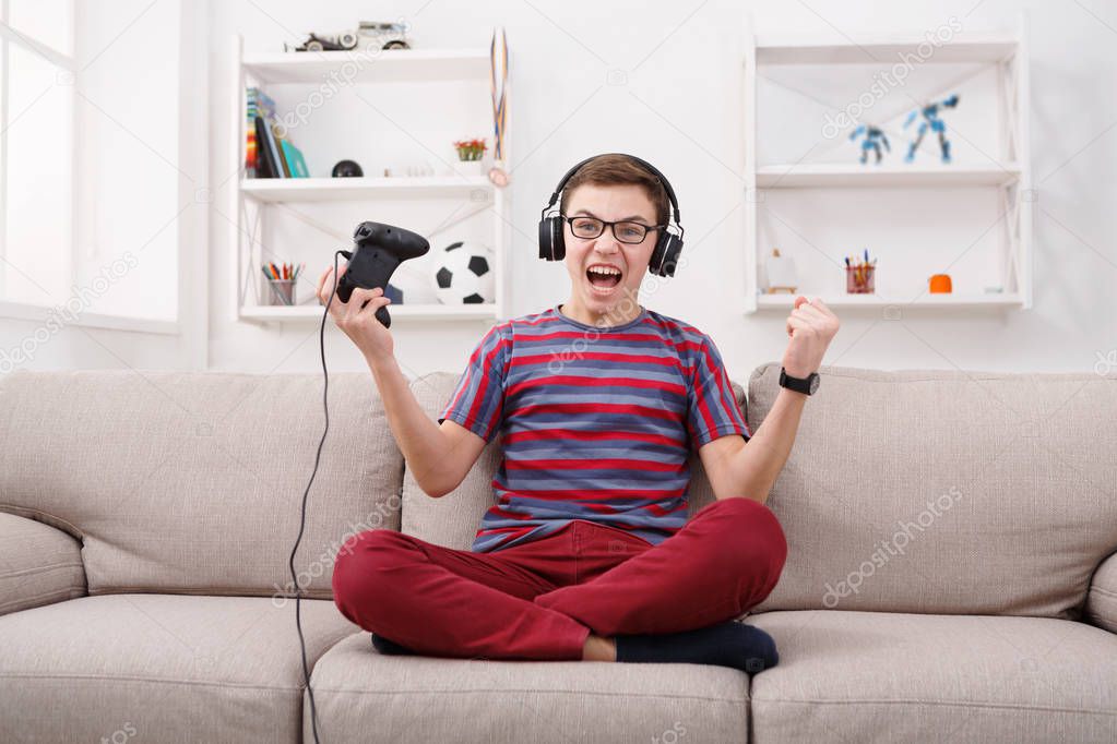 Excited teenage boy playing video game at home