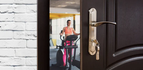 Entrance to gym in fitness club, opened door with woman on elliptical trainer