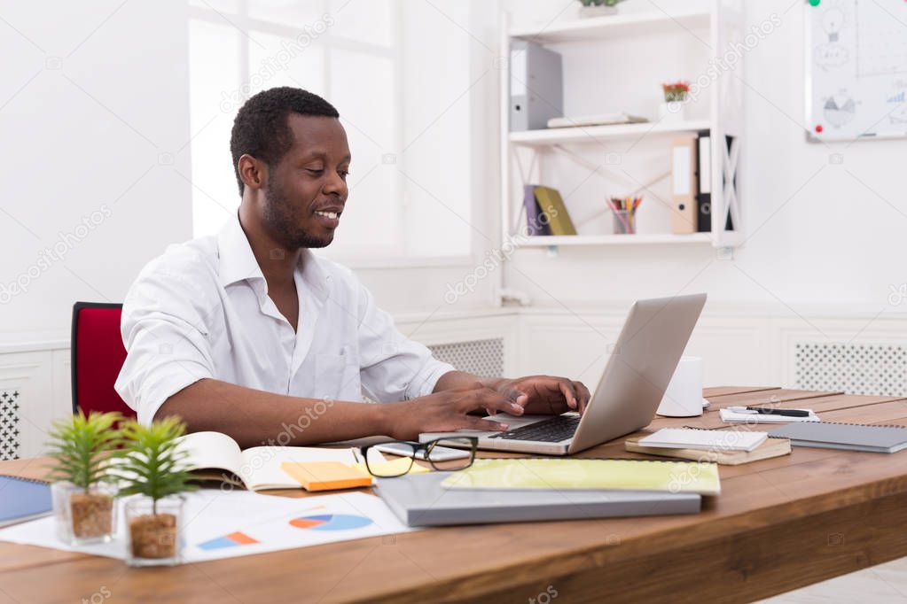Young black businessman working with laptop in modern white office