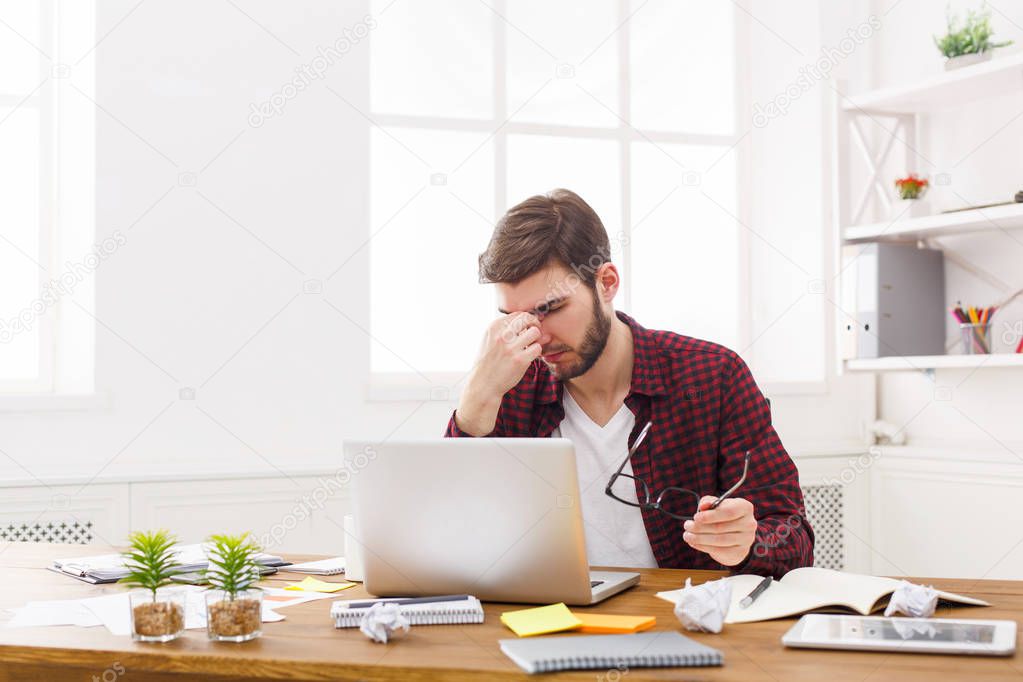 Tired, overworking businessman with laptop in modern white office