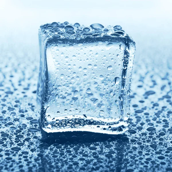 Transparenter Eiswürfel mit Reflexion auf blauem Glas mit Wassertropfen — Stockfoto