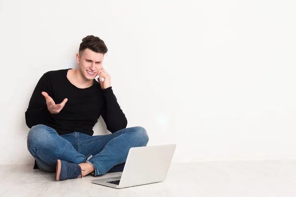 Jonge man freelancer in casual met laptop praten op mobiele telefoon — Stockfoto