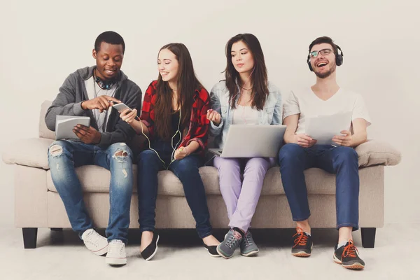 Diversos estudantes usando gadgets, sentar-se no sofá — Fotografia de Stock