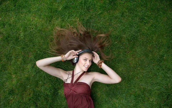 Pretty young girl listen music in headphones lying on grass — Stock Photo, Image