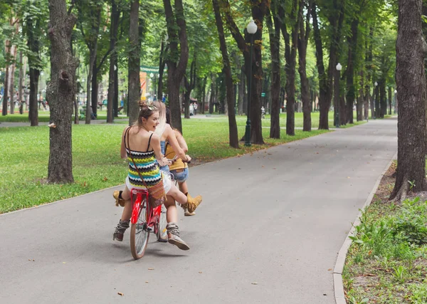 Felice boho chic ragazze cavalcare insieme su biciclette nel parco — Foto Stock