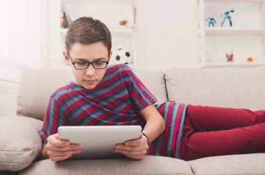 Genç çocuk evde kanepede dijital tablet kullanma