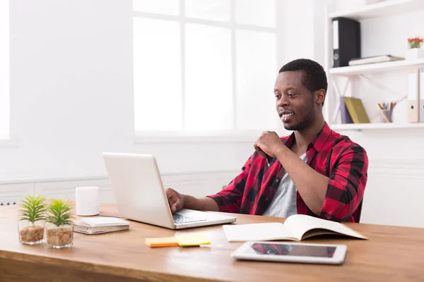 Homme d'affaires noir souriant dans un bureau décontracté, travailler avec un ordinateur portable — Photo