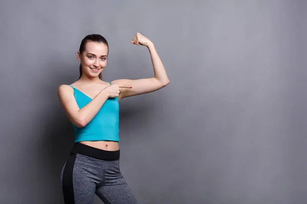 Sonriente mujer fitness muestra su mano muscular —  Fotos de Stock