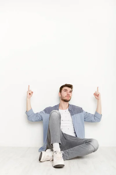 Oturma ve yukarı doğru elleriyle işaret eden genç adam — Stok fotoğraf