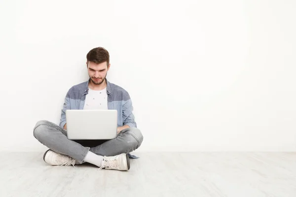 Молодой человек работает на ноутбуке, сидя на полу — стоковое фото