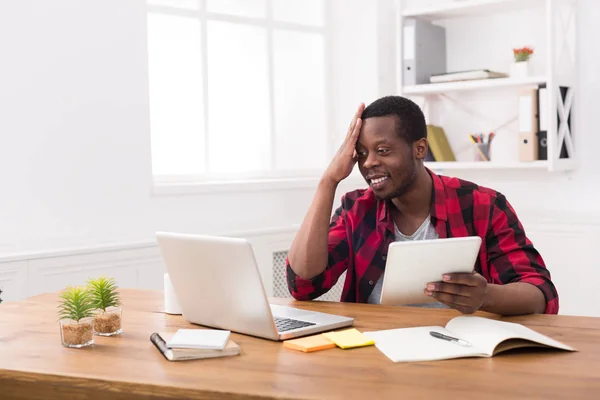 Homme d'affaires noir dans un bureau décontracté, travailler à la fois sur ordinateur portable et tablette — Photo