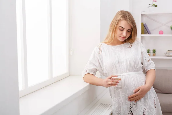 Wanita hamil dengan segelas air duduk di sofa — Stok Foto