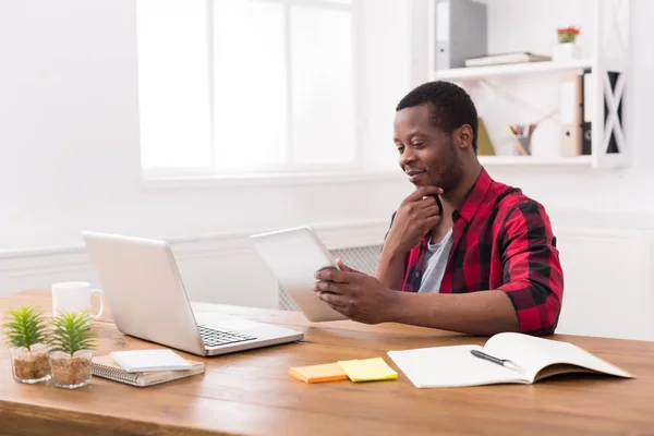Hombre de negocios negro en la oficina informal, el trabajo con el ordenador portátil y la tableta —  Fotos de Stock