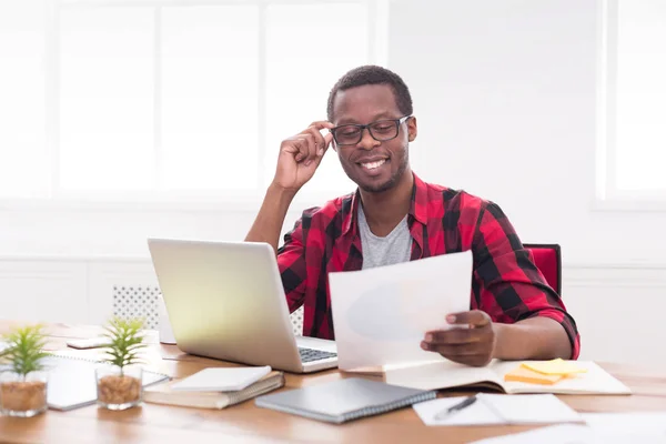 Homem de negócios preto no escritório casual, local de trabalho com laptop e papelada — Fotografia de Stock