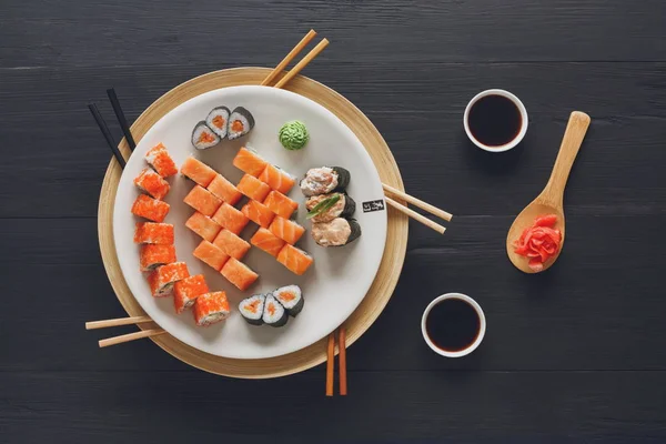 Lax sushi och rullar på svart bakgrund, ovanifrån — Stockfoto