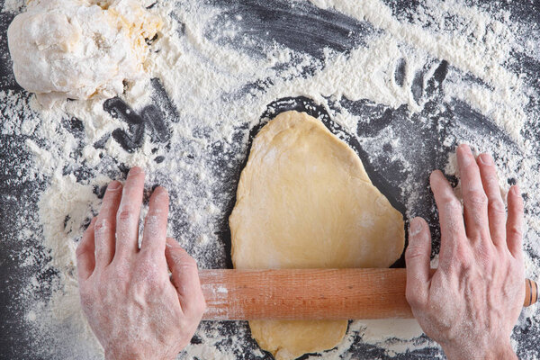 Baking concept. Hands top view roll dough on black background. Male baker