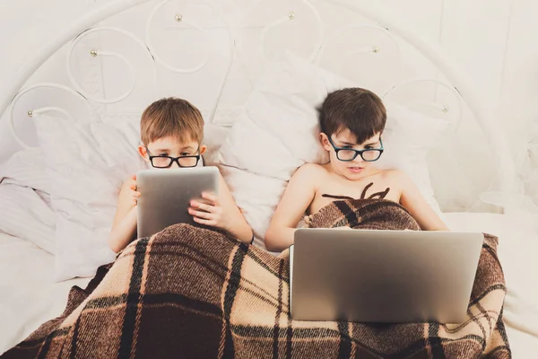 Dos muchachos juegan en el portátil y la tableta con el perro en la cama — Foto de Stock