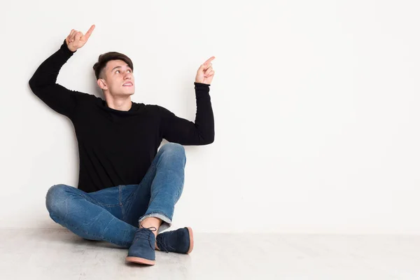 Joven apunta hacia arriba en el fondo del estudio blanco . —  Fotos de Stock