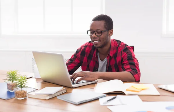 Happy black podnikatel v běžné kanceláři, práce s notebookem — Stock fotografie