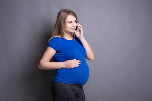 Усміхнена вагітна жінка говорить на своєму смартфоні — стокове фото